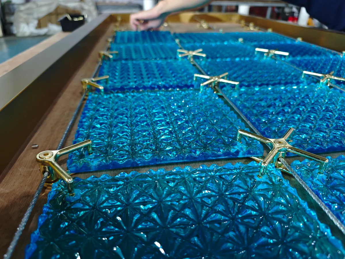 Gold-colored four-arm connectors and metal cables between blue textured crystal panels on a workshop table.